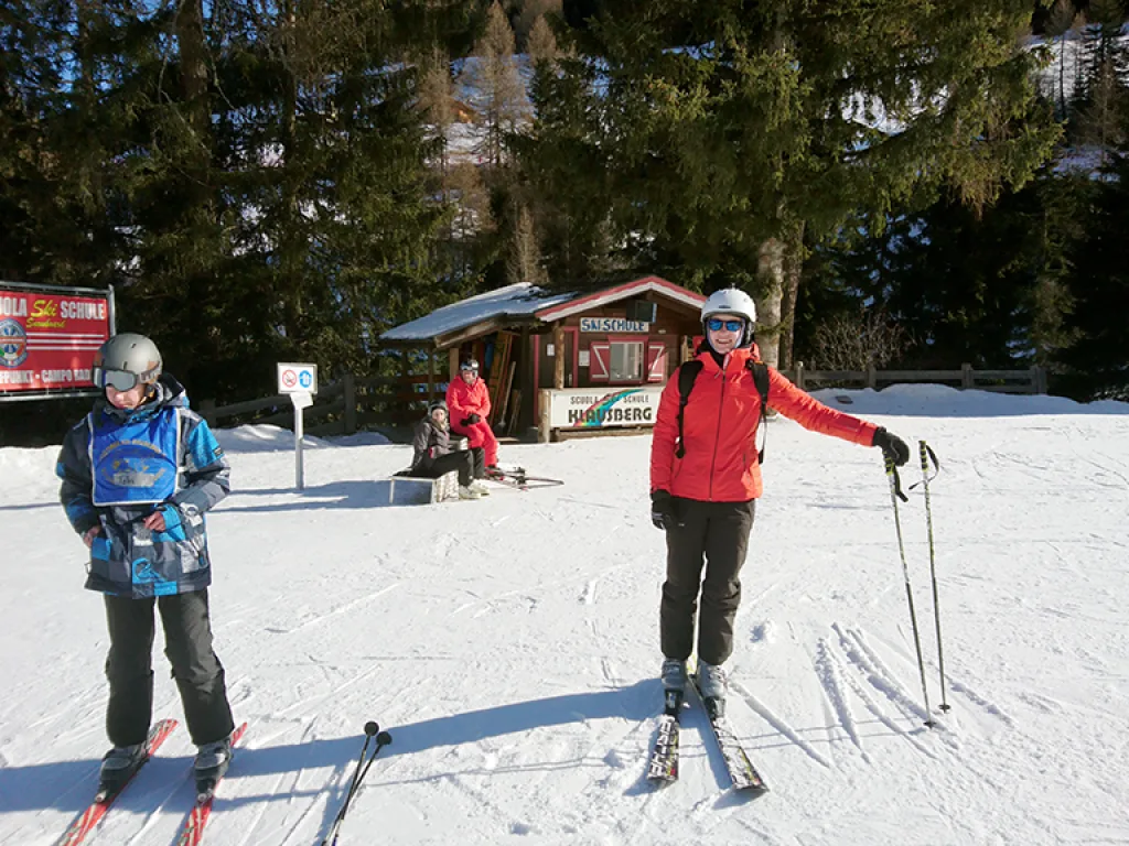 Zwei Skifahrende stehen vor einer Hütte am Pistenrand.